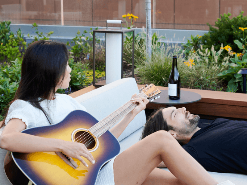 A woman relaxes in a lounge chair on the patio while playing an acoustic guitar