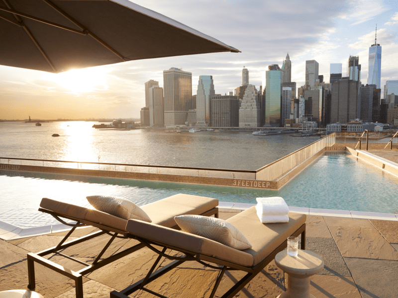 Relaxing rooftop pool area feautring reclined lounge chairs with a view of the skyline