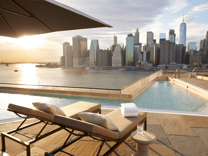 Relaxing rooftop pool area feautring reclined lounge chairs with a view of the skyline