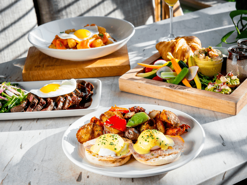Various breakfast dishes pictured.  From left to right, steak and eggs, a breakfast skillet, eggs benedict, and a compliment of fresh veggies, croissants, and avocado toast