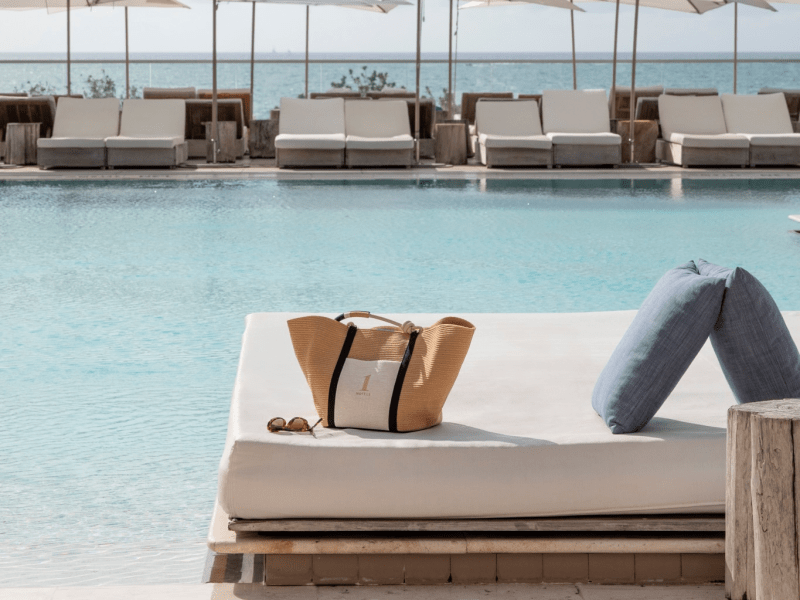 A white mattress and a Rothy's bag are placed on the edge of a pool, creating a serene outdoor setting.
