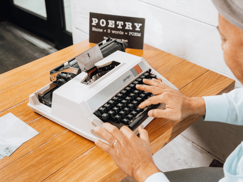 A man sits at a desk using a Super deluxe typewriter