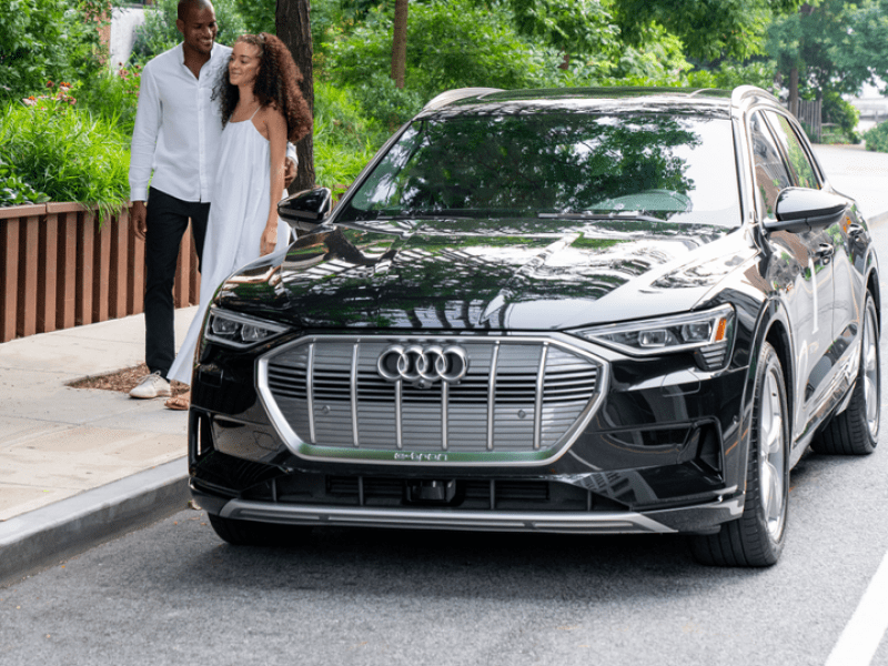 Two people standing beside a black Audi