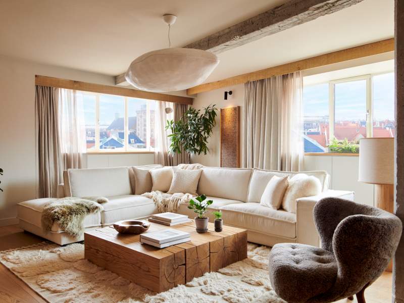 A well-appointed living room with two large windows, an area rug and coffee table, a sectional and arm chair