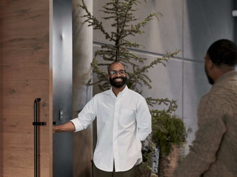 Person holding a large wooden door open for another person walking through it