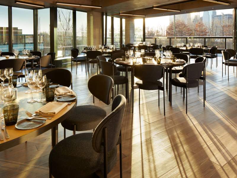 Aster Social Evening spacious room with large round wooden tables each set for eight individuals