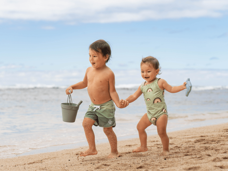 Two children holding each others hands and running down a beach