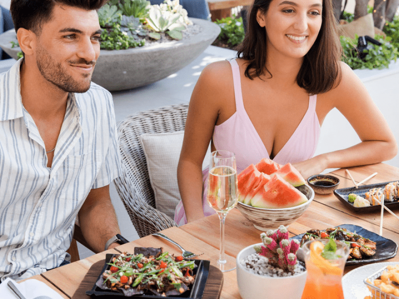 Two people sitting at a table with plates of food and drink