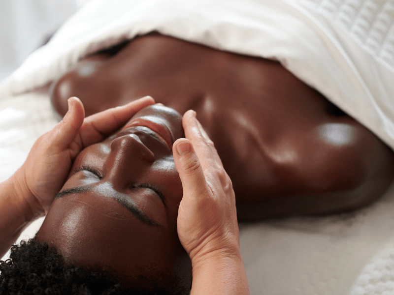 A woman lying face up on a massage bed receives a relaxing spa facial 