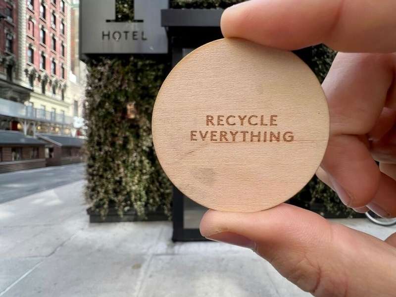 Picture from @farmernick holding a round wood piece saying "Recycle Everything" With the 1Hotels on the background 