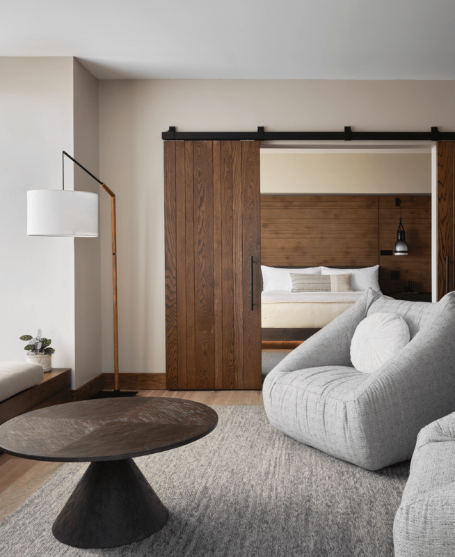 Two large gray chairs and a sofa positioned around a dark brown circular coffee table, overlooking views of the water