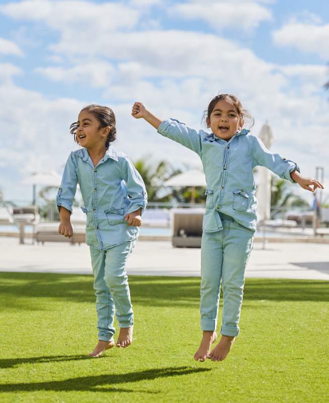 Deux petits enfants vêtus de tenues en jean assorties sautent et sourient à l'appareil photo.