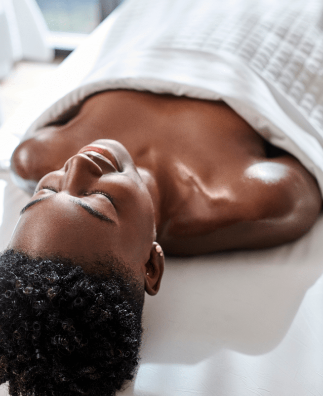 A woman lying face up on a massage table, eyes closed, relaxing