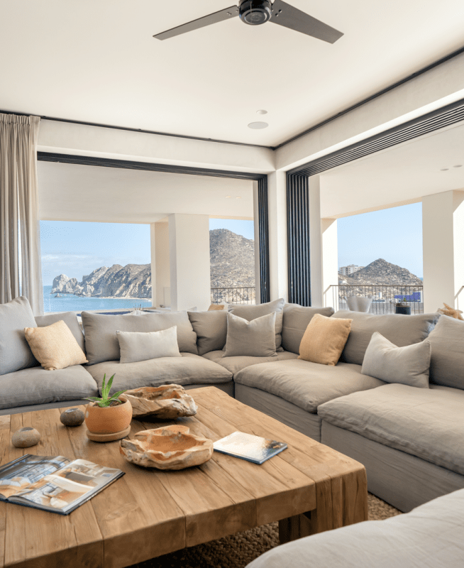 Windows with a panoramic view of the seascape outside line a large room with a wrap around sectional