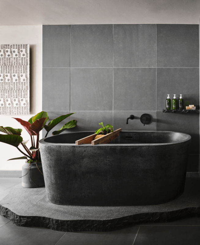 A large granite bathtub sits atop another slate of granite with a gray tile backdrop