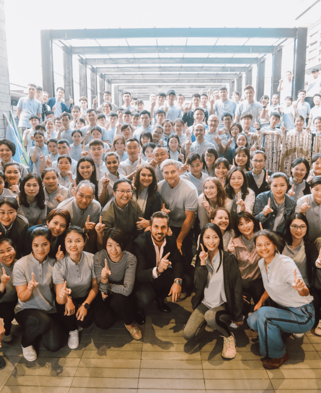 Group of people huddled together for a photo holding up their index fingers