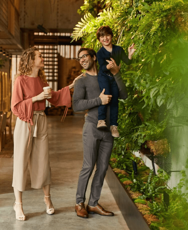 Man holding child up towards plant wall 