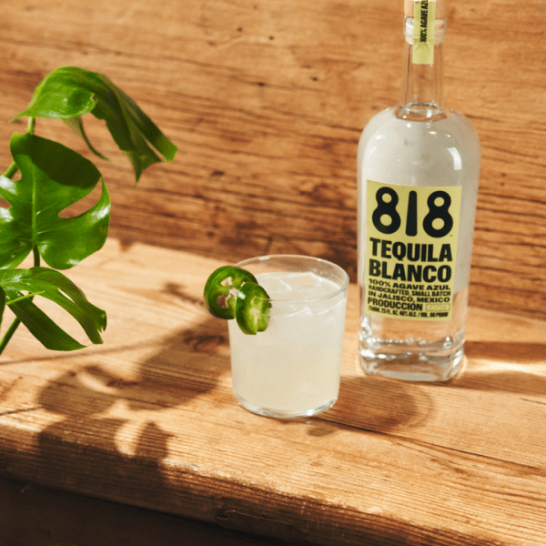 Margarita with jalapeno garnish next to a bottle of 818 tequila