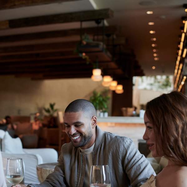 A man and woman laugh while holding their wine glasses in front of them