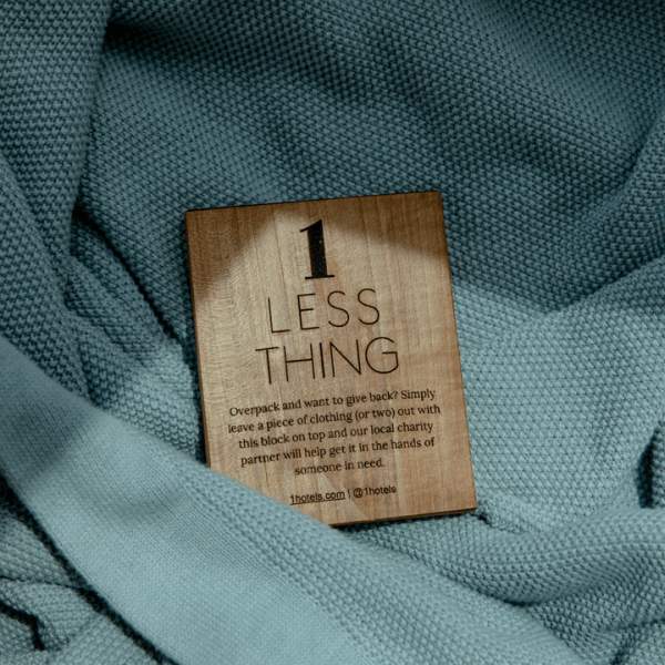 A wooden block with the text 1 Less Thing pictured nestled into a light blue sweater