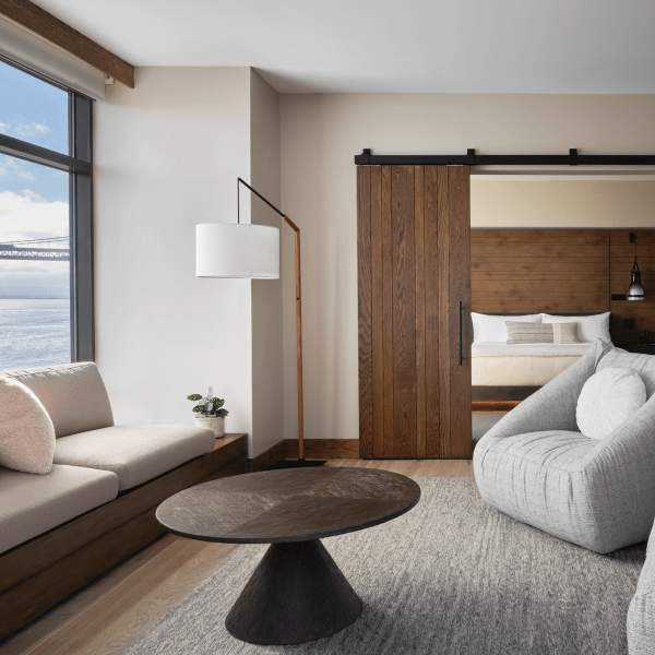 Two large gray chairs and a sofa positioned around a dark brown circular coffee table, overlooking views of the water