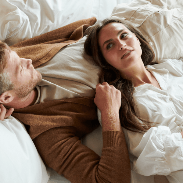 A couple, one woman with her head laying on a man, rest together in a 1 Hotels bed