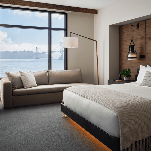 A king size bed sits center of the room, while a sofa sits positioned against a window overlooking the water