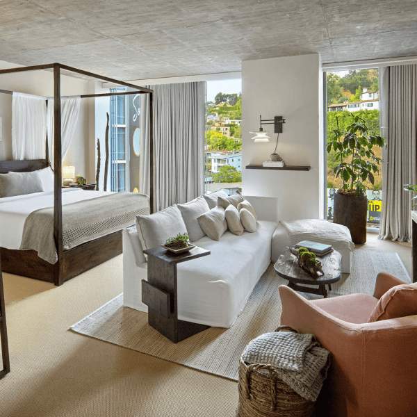 Un lit king size est placé sous un cadre à baldaquin.  Un canapé blanc est placé devant le lit, face à un téléviseur.