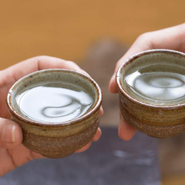 Duas pessoas com copos de saquê nas mãos