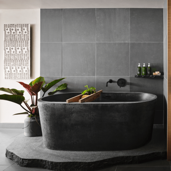 A large granite bathtub sits atop another slate of granite with a gray tile backdrop