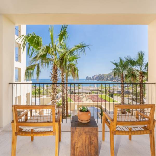 Two wooden patio chairs face outwards on the patio overlooking the beach and sea
