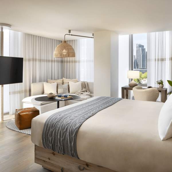 A king size bed centered in the middle of the room positioned in front of the television with views of the city beyond