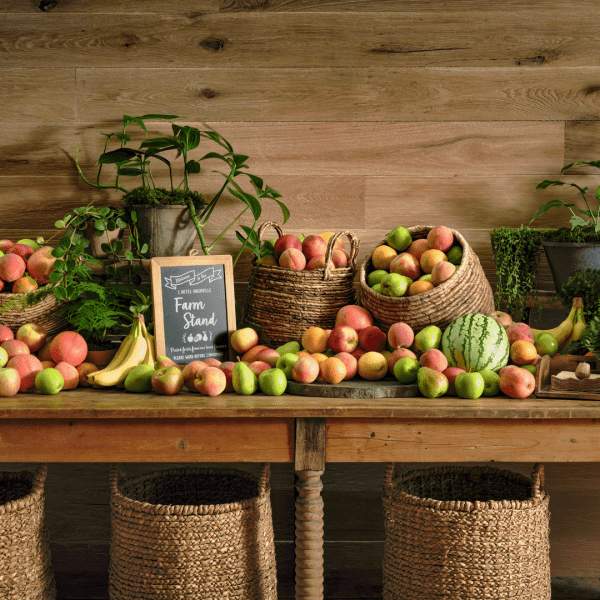Un lungo tavolo di legno rustico con un cartello con la scritta Farm Stand è circondato da una pletora di mele di diverse varietà.