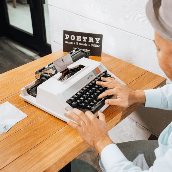 A man sits at a desk using a Super deluxe typewriter