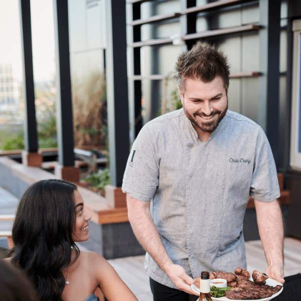 Culinary director Chris Crary delivers food to a table of excited looking guests at 1 Hotels Nashville