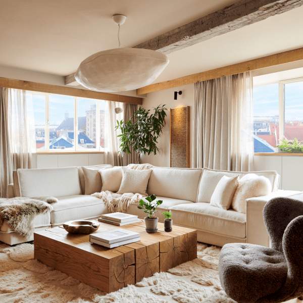 A well-appointed living room with two large windows, an area rug and coffee table, a sectional and arm chair