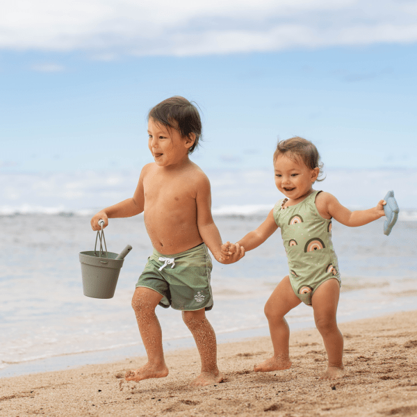 Two children holding each others hands and running down a beach