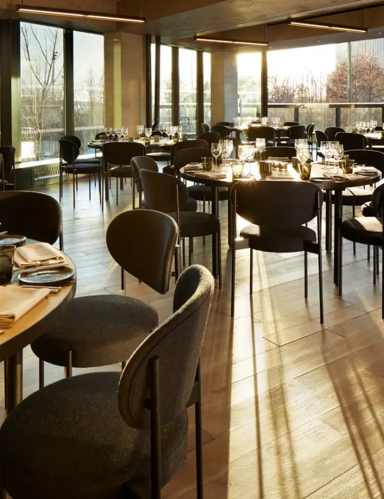 Aster Social Evening spacious room with large round wooden tables each set for eight individuals