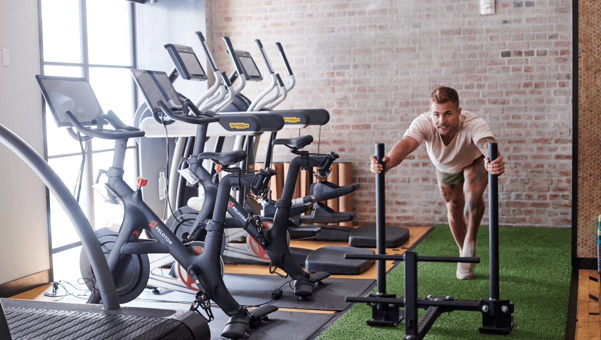 Gym with treadmills and man pushing weights on turf