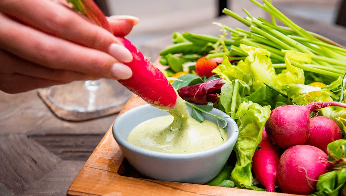 Person dipping a carrot in an avocado dressing