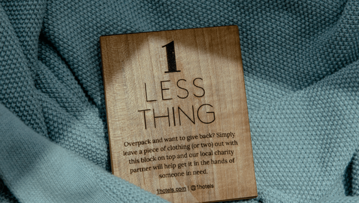 A wooden block with the text 1 Less Thing pictured nestled into a light blue sweater