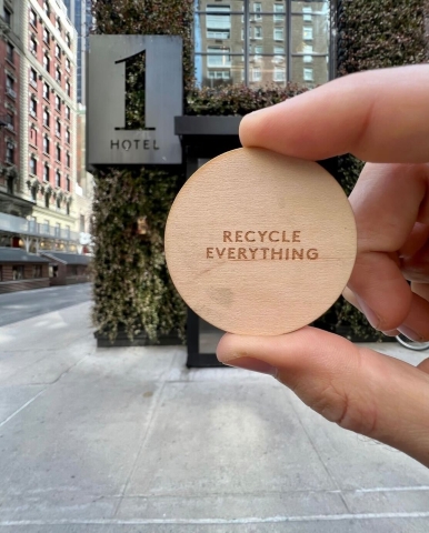 Picture from @farmernick holding a round wood piece saying "Recycle Everything" With the 1Hotels on the background 