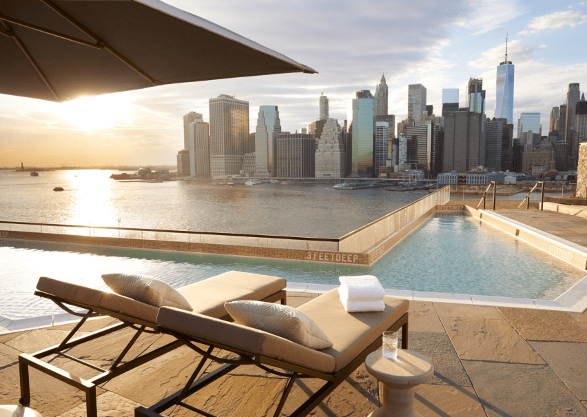 Relaxing rooftop pool area feautring reclined lounge chairs with a view of the skyline