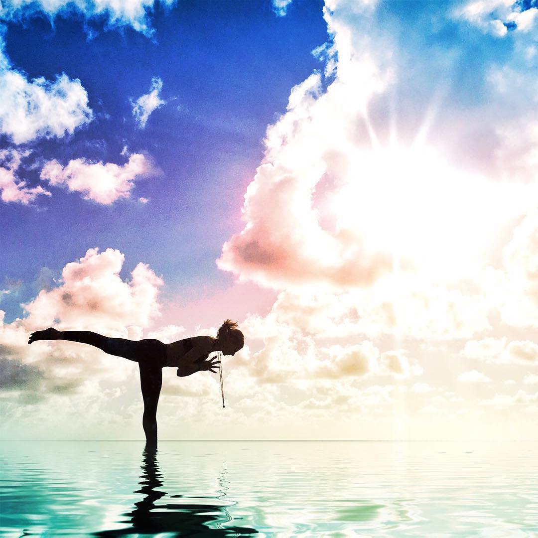 A woman doing yoga in shallow water at sunrise