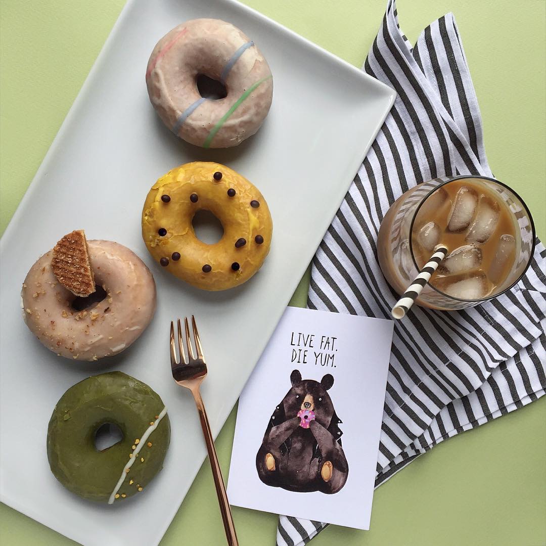 Four different artisinal doughnuts on a plate next to a card that says EAT FAT. DIE YUM.
