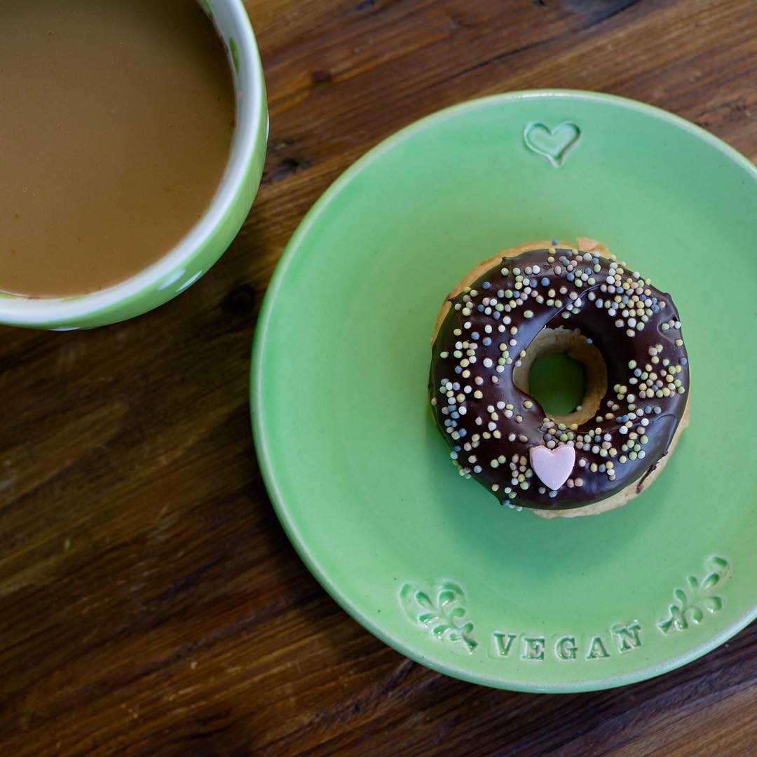 A chocolate glazed doughnut on a green plate that says VEGAN