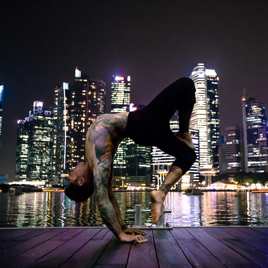 A man doing yoga on a dock in front of a city skyline at night