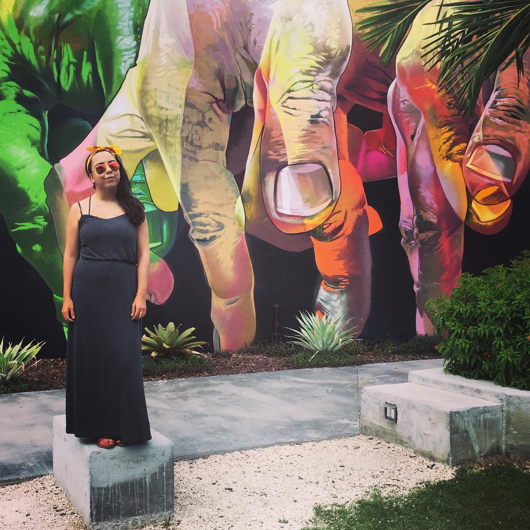 A woman standing on a cement block in front of a mural of hands