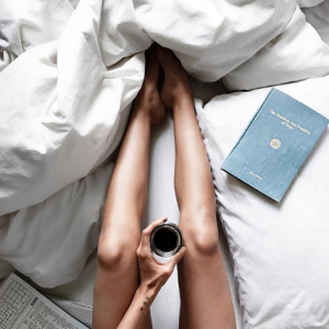 A woman sitting in bed with a coffee and a book