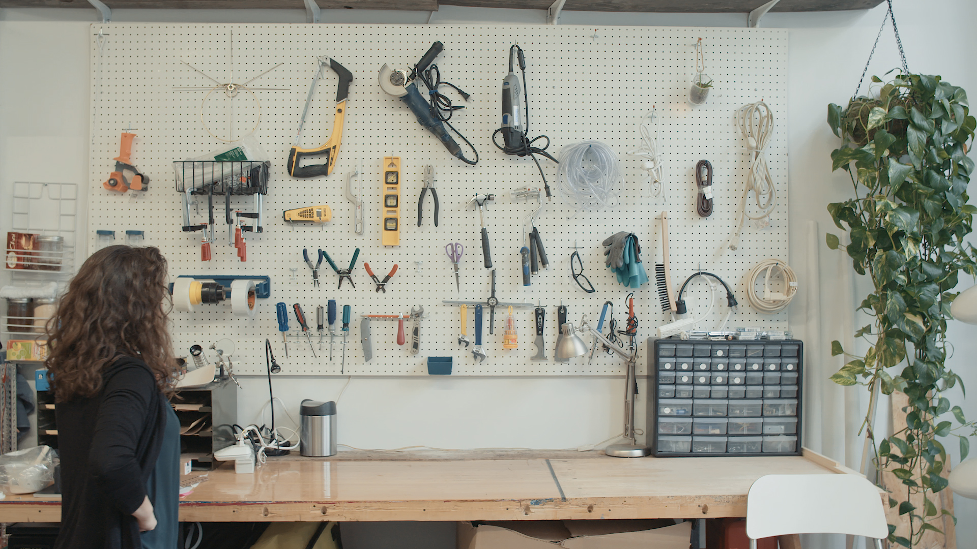 A woman looking at a wall of hanging tools in a workspace